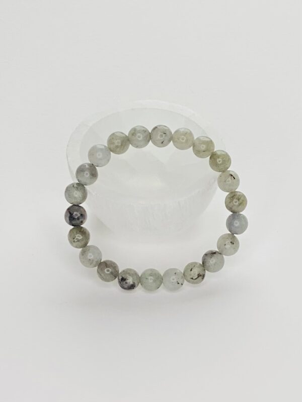 A bracelet of grey and white beads on a clear surface.