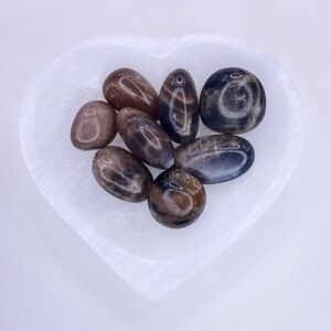 A heart shaped glass bowl with Black Moonstone Tumbled Stones in it.