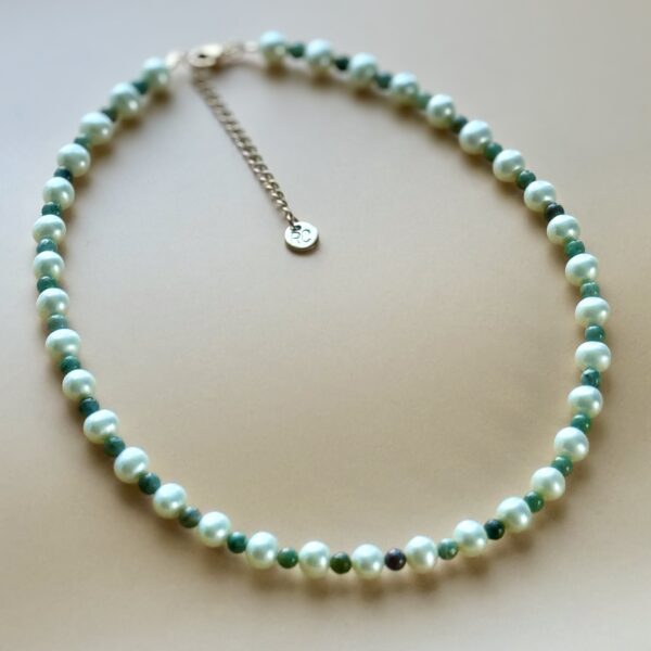 Pearl and green stone necklace on beige background.