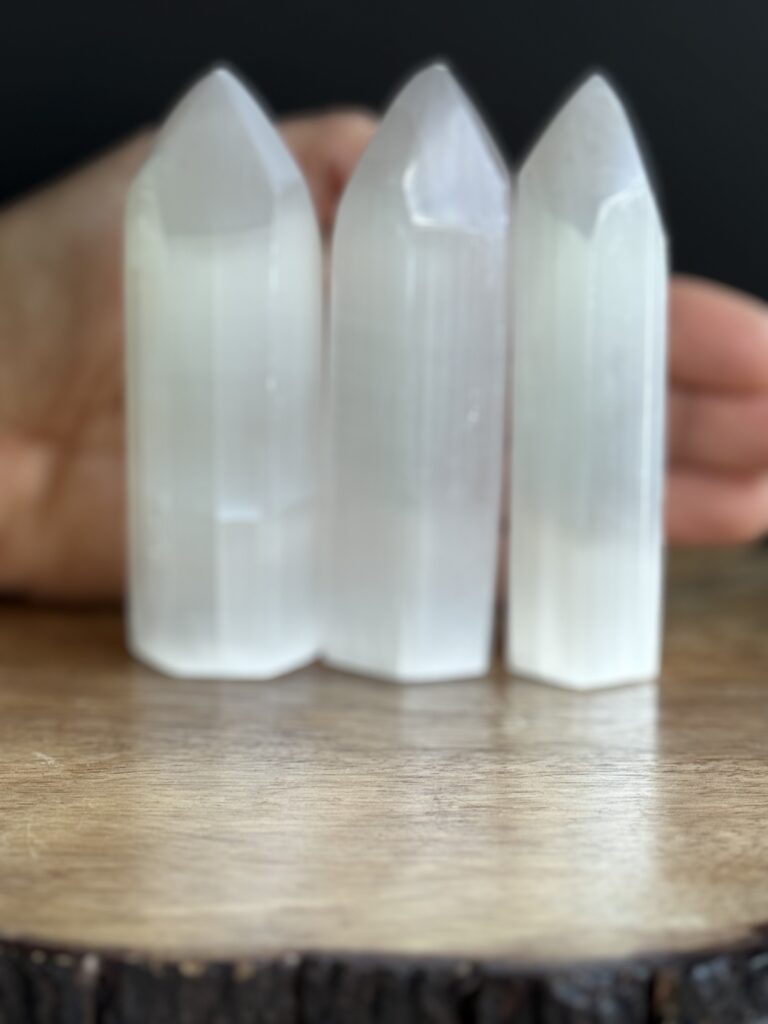 Three white selenite crystal points on wood.