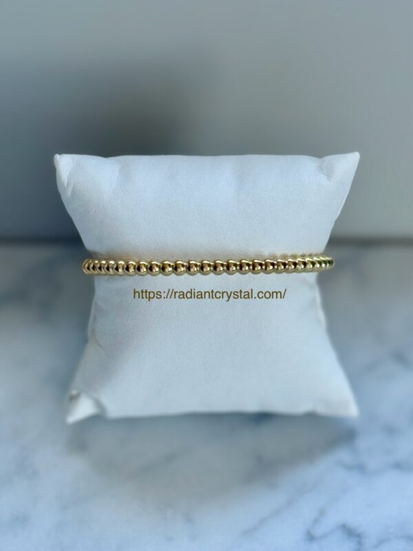 Gold beaded bracelet on white cushion.